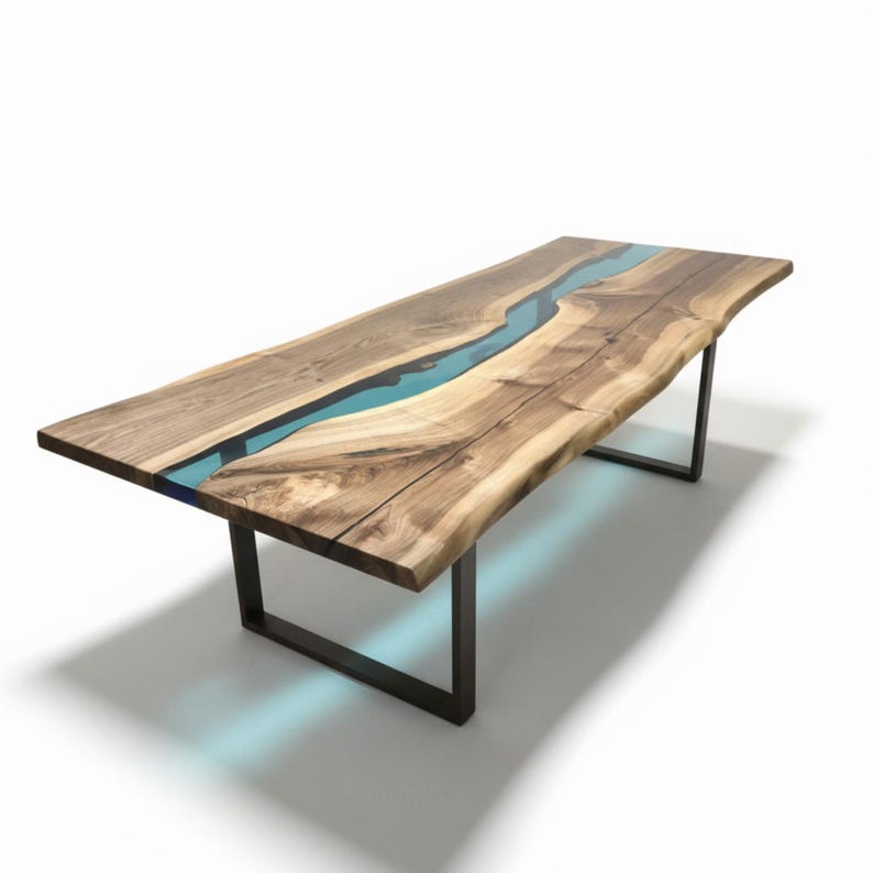 Puede incluir: Una mesa de comedor rectangular con dos tablones de madera natural de borde vivo unidos por una incrustaci&oacute;n central de resina azul transl&uacute;cida. La mesa se apoya sobre dos patas de metal negro en forma de U como base.