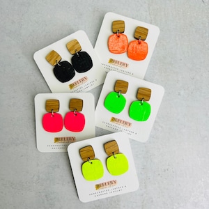 May include: Five pairs of neon colored earrings with wooden posts. The earrings are displayed on white cards with the text "BEELERY Handmade with Love" and "HANDCRAFTED LEATHER & MACRAME JEWELRY".