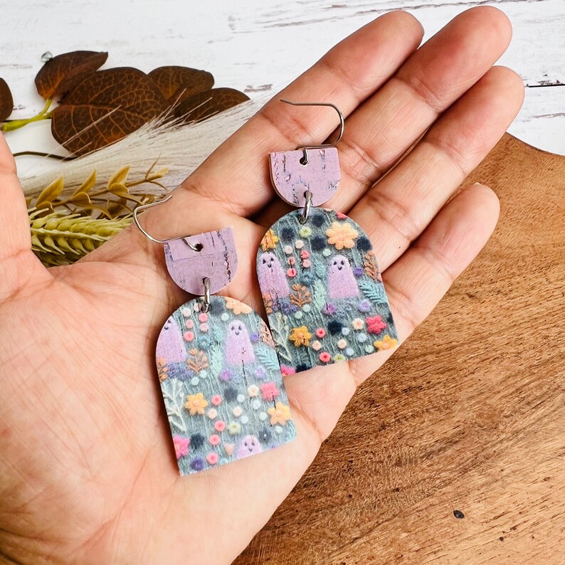 May include: A pair of purple and green ghost earrings with a floral pattern. The earrings are made of cork and have a silver hook.