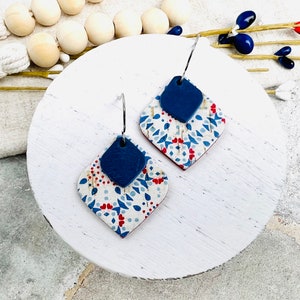 May include: A pair of blue and white patterned earrings with a blue diamond-shaped accent. The earrings are made of polymer clay and have silver hooks.