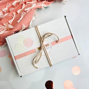 May include: A white gift box with a pink ribbon and twine bow. The box has a sticker that says "Bakery" with a heart and the text "Gifts with love".
