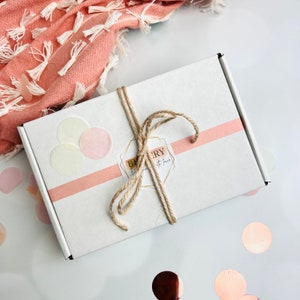 May include: A white gift box with a pink ribbon and a brown twine bow. The box has a sticker that says "Bakery with love". There are pink and white paper circles on the box.