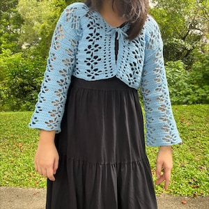 May include: A light blue crocheted cardigan with a tie front and long sleeves. The cardigan is cropped and has a delicate openwork pattern.