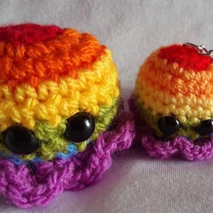 May include: Two crocheted rainbow octopus plushies with black eyes. The larger octopus has a purple tentacle base and the smaller octopus has a purple tentacle base and a silver keychain.