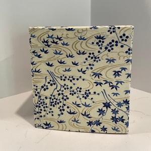 May include: A white journal with a blue and gold floral pattern. The cover features a repeating design of stylized leaves, flowers, and swirls.