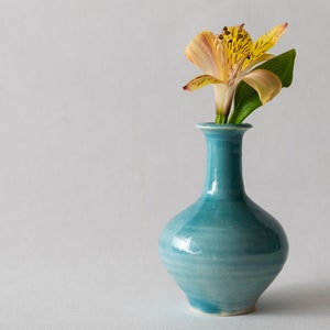 Pode incluir: Uma única flor amarela e marrom com folhas verdes em um vaso de cerâmica azul.