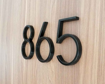 Peut inclure: Numéros de maison noirs 865 sur un fond en bois.