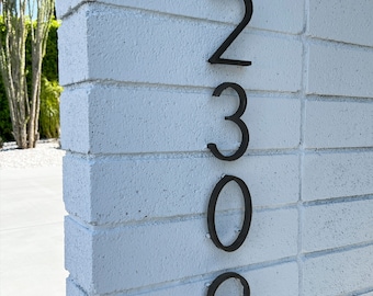 Peut inclure: Numéros de maison en métal noir 2309 fixés à un mur en briques blanches.
