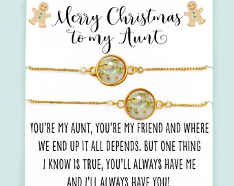 May include: A white card with gold glitter and a message that reads "Merry Christmas to my Aunt." The card is accompanied by two gold chain bracelets with a clear round charm containing gold glitter.