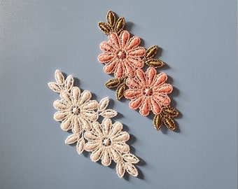 May include: Two delicate lace flower appliques, one in white and one in pink, with gold accents. These floral embellishments are perfect for adding a touch of elegance to clothing, crafts, or home decor.