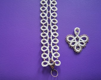 May include: A white crocheted bracelet with a silver clasp and a matching white crocheted heart charm on a purple background.