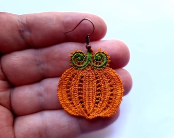 May include: Orange and green pumpkin-shaped earrings made of crocheted thread. The earrings are hanging from a brown metal hook.