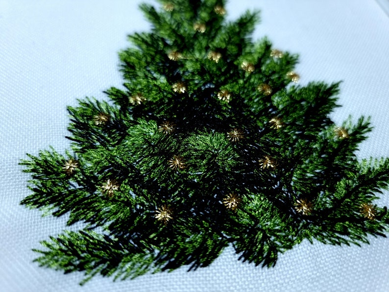 May include: Embroidered Christmas tree design with green foliage and gold accents. The tree is stitched on a white fabric background.