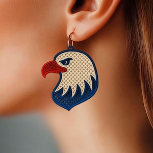 May include: Embroidered eagle head earrings with red, white, and blue details. The earrings feature a gold hoop and a detailed design of an eagle's head, showcasing a patriotic theme.