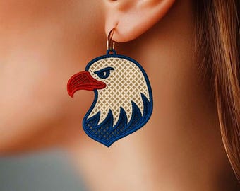 Puede incluir: Pendientes bordados con cabeza de águila con detalles rojos, blancos y azules. Los pendientes presentan un aro dorado y un diseño detallado de la cabeza de un águila, mostrando un tema patriótico.