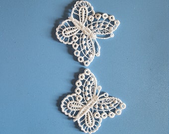 May include: Two white lace butterfly appliques on a blue background.