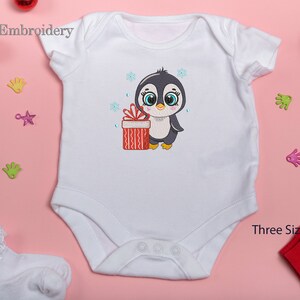May include: White baby onesie with an embroidered design of a penguin holding a red and white gift box. The penguin is wearing a black hat and has blue eyes. The design is surrounded by snowflakes.