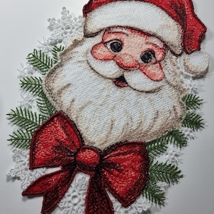 May include: Embroidered Christmas ornament featuring a red-hatted Santa Claus with a white beard and a red bow. The ornament is surrounded by white snowflakes and green pine branches.
