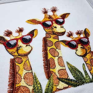Peut inclure: Trois girafes brodées portant des lunettes de soleil, avec des taches brunes et jaunes, se tiennent devant des feuilles vertes.