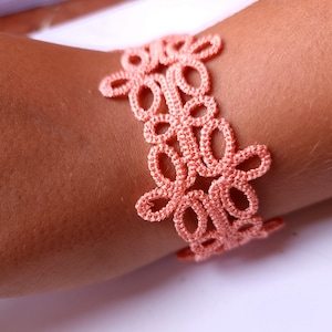 Könnte beinhalten: Ein zartes, peachfarbenes Häkelarmband mit Blumenmuster.