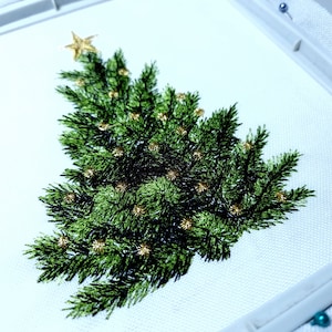 May include: Embroidered Christmas tree design on white fabric with gold accents. The tree is green and has a star on top.