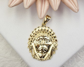 May include: Gold pendant featuring a detailed profile of a Native American man wearing a headdress. The pendant is a round shape and has a textured surface.