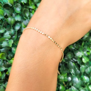 May include: A delicate gold chain bracelet with small round links. The bracelet is shown on a person's wrist.