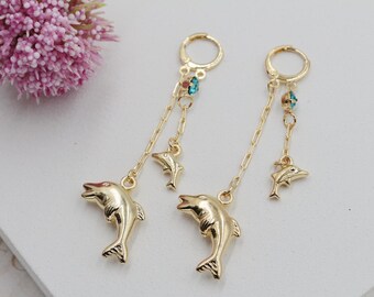 May include: Gold tone dangle earrings with a turquoise gemstone and two gold dolphin charms.