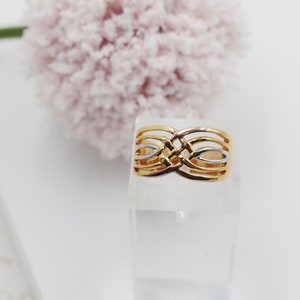 May include: A gold ring with a woven design featuring alternating bands of yellow and white gold.