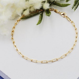 May include: A gold chain bracelet with a lobster clasp closure. The chain is made of small, rectangular links.