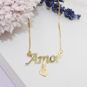 May include: A gold necklace with a pendant that says "Amor" with a small heart charm.