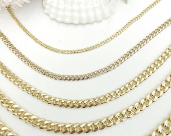 May include: A collection of gold-colored curb chain necklaces of varying thicknesses. The chains are displayed on a white surface, showcasing their polished, reflective finish. The necklaces are arranged in a layered presentation.