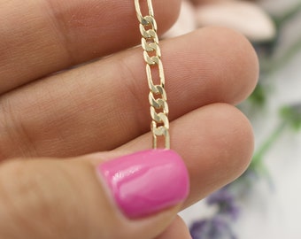 May include: A close-up of a gold chain necklace with a curb link style. The chain is held in a hand with pink nail polish.
