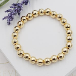 May include: A gold beaded bracelet with round beads. The bracelet is on a white surface.