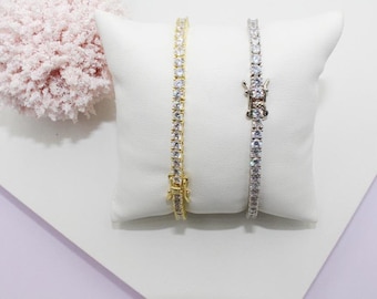 Puede incluir: Dos pulseras de tenis, una dorada y otra plateada, con piedras de circonita cúbica transparentes. Las pulseras se muestran sobre una almohada blanca.