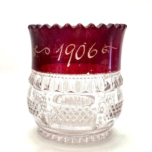 May include: A white ceramic mug with a black handle and the text "But First, Coffee" in a bold, black font. The mug is set against a blurred background, suggesting a cozy setting.