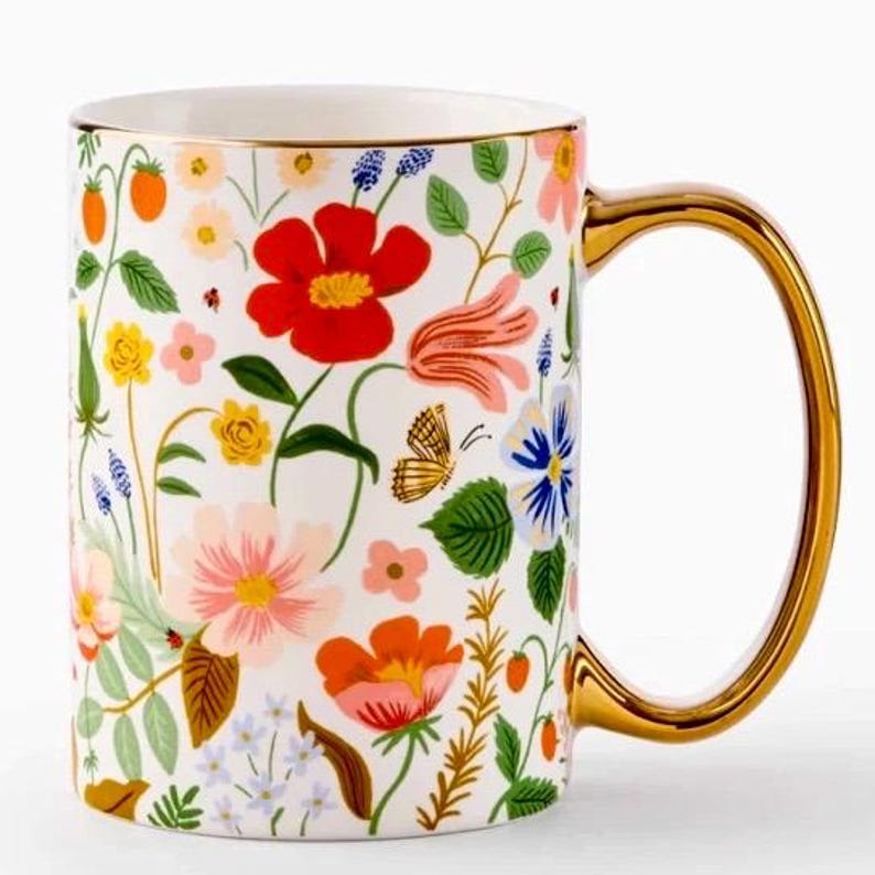 May include: White ceramic mug with a gold handle and rim, adorned with a colorful floral pattern. The design includes red, pink, and orange flowers, green leaves, and a butterfly. The mug is a standard size for coffee or tea.