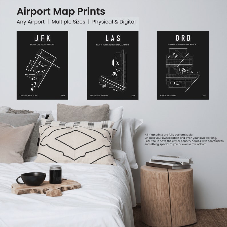 May include: Three black and white airport map prints with the airport codes JFK, LAS, and ORD. The prints are displayed on a white wall above a white bed with pillows and a wooden side table.