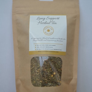 Może przedstawiać: Brązowa papierowa torebka z przezroczystym okienkiem, które ukazuje mieszankę suszonych ziół. Torebka ma etykietę z napisem "Lung Support Herbal Tea" z logo "Golden Age Remedies". Etykieta informuje również, że herbata jest synergistyczną mieszanką tradycyjnych ziół dla zdrowia płuc i funkcji oddechowej. Jest to 100% naturalny suplement diety, 100% składników organicznych i nie zawiera żadnych dodatków ani sztucznych konserwantów. Adres strony internetowej to www.goldenageremdies.com.