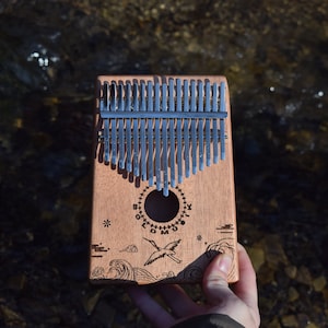 A kalimba, same design, ocean waves with bird. The picture is someone holding the kalimba with one hand to show the scale.