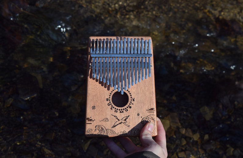 A kalimba, same design, ocean waves with bird. The picture is someone holding the kalimba with one hand to show the scale.