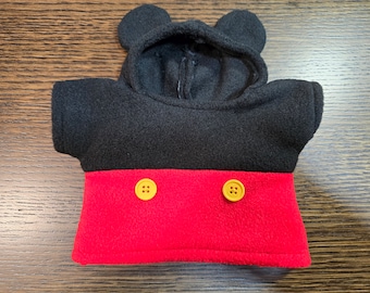 Könnte beinhalten: Ein schwarzer und roter Fleece-Hoodie mit Mickey Mouse Ohren. Der obere Teil ist schwarz und der untere Teil ist rot mit zwei gelben Knöpfen. Die Kapuze ist befestigt und hat zwei abgerundete Ohren.