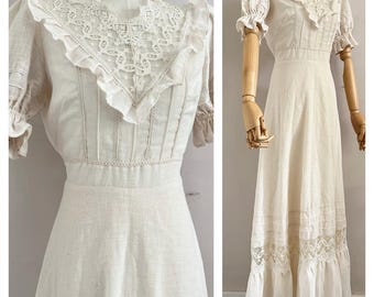 May include: A cream-colored vintage dress with a high, lace-trimmed collar and short, puffed sleeves. The dress features a fitted bodice with vertical pleats and a flowing skirt with lace detailing at the hem. The dress is displayed on a mannequin.