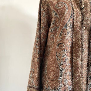May include: A brown embroidered jacket with a paisley pattern. The jacket has a mandarin collar and a button closure.