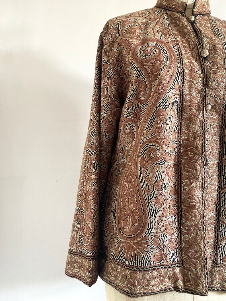 May include: A brown embroidered jacket with a paisley pattern. The jacket has a mandarin collar and a button closure.