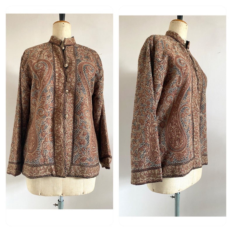 May include: A brown paisley patterned jacket with a mandarin collar and button closure. The jacket has long sleeves and a fitted silhouette.