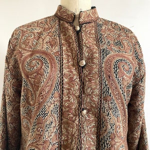 May include: A brown and black embroidered jacket with a mandarin collar and button closure. The jacket is made of a soft, luxurious fabric and features intricate floral patterns.