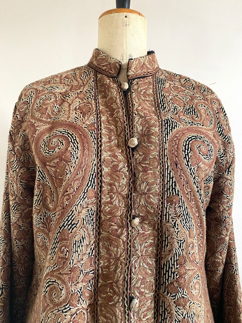 May include: A brown and black embroidered jacket with a mandarin collar and button closure. The jacket is made of a soft, luxurious fabric and features intricate floral patterns.