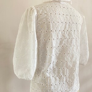 Puede incluir: Blusa blanca de algod&oacute;n con un delicado estampado floral y un cuello con volantes. La blusa tiene un corte holgado y mangas 3/4.