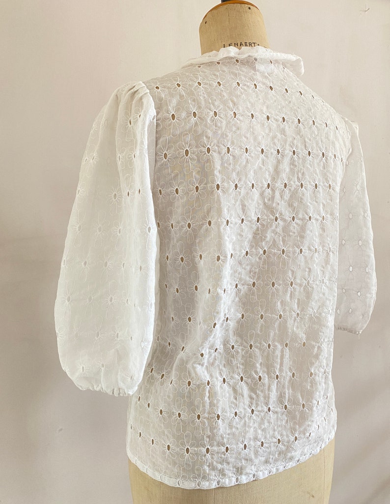 Puede incluir: Blusa blanca de algod&oacute;n con un delicado estampado floral y un cuello con volantes. La blusa tiene un corte holgado y mangas 3/4.